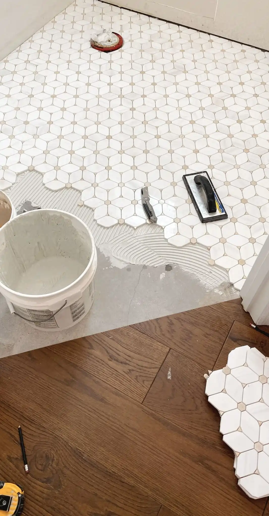Tile installer laying white hexagon mosaic floor tiles with adhesive mortar mid-installation