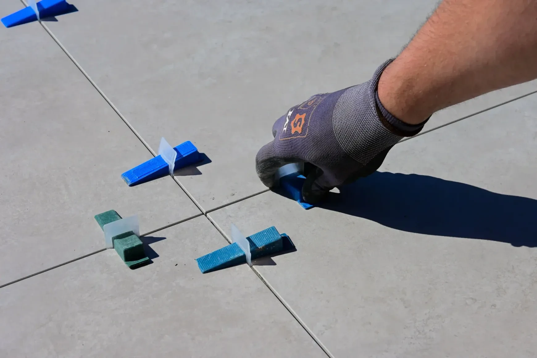 Tile installer using blue leveling clips and wedges on large-format floor tiles
